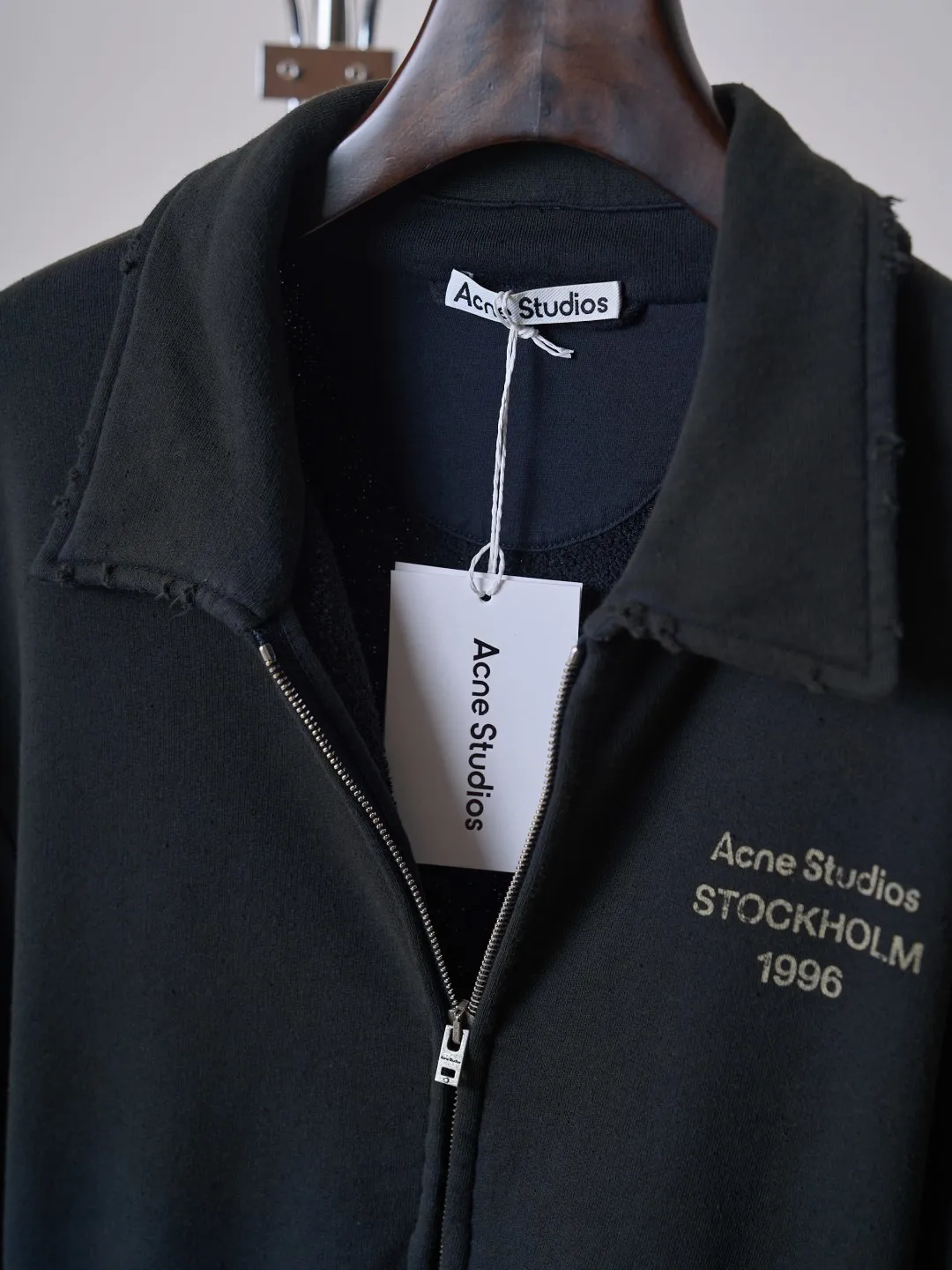[Real auction] Acne Studios Retro distressed letter print zipper jacket [In Stock] Logo stamp at front, side-seam pockets, and ribbed cuffs and hem. Regular fit, just above the waist. It adopts a 3-strand composite fleece structure with 32 counts for the top layer and 40 counts for the bottom layer, with a weight of g/㎡. The 32-count yarn on the top layer is fine and smooth, giving the surface a smooth touch and excellent anti-pilling properties; the 40-count 3-ply yarn on the bottom layer is treated with a raising process to form a rich and soft fluff layer, providing excellent warmth and skin-friendly wrapping. With 21 2×2 ribs, the g/㎡ weight ensures that the collar, cuffs and hem have excellent tensile fatigue resistance and shape retention capabilities. During piece dyeing, the entire fabric is immersed in the dye vat after weaving, and the dye molecules fully penetrate into the fibers, ensuring full, deep colors and excellent color fastness. Each batch of dyeing produces subtle differences, making the color tone of the single product unique. On this basis, the paint is sprayed irregularly on the surface of the garment through manual spray painting to create a splash-like retro effect. The distressed processing of holes causes the color to fade and mottle in parts. The ribbed trim is also treated to form slight whitening and fluffing, which visually echoes the spray-painted effect on the body, making the new clothes appear as if they have been worn for a long time and exposed to the sun. The front logo stamp uses a slurry printing process. The printing slurry contains a special microcapsule foaming agent. After being baked at high temperature, the slurry layer expands to form three-dimensional bulges, and the surface presents a granular texture similar to inkjet paint. This process simulates the effect of random drops of pigment after being atomized during spray gun spraying. The edges of the pattern present a natural feathering transition, rather than the rigid boundaries of glue printing. The printing surface has a fine graininess and soft elasticity to the touch, forming a closed loop of the process with the distressed effect of the spray painting on the body.